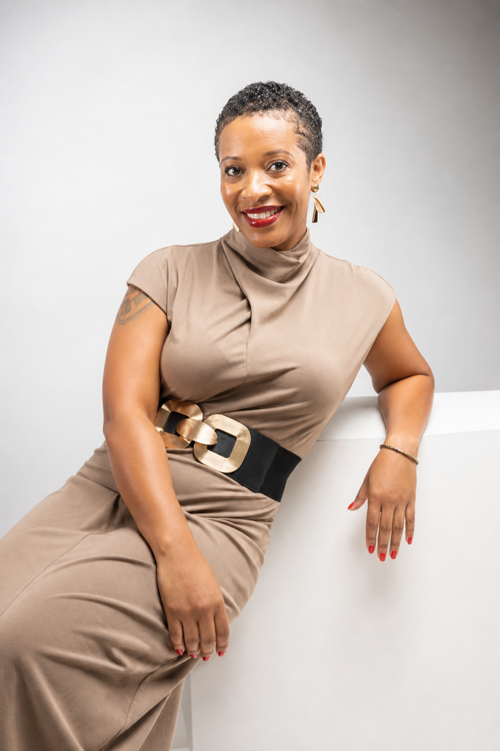 Lasheika Brown, Founder and Principal Consultant of Fanik Consulting, seated in a tan dress with a gold-buckled belt